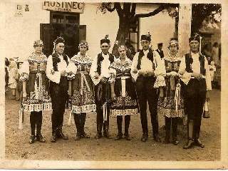 Fotografie ukazuje stárky a stárkyně o hodech před starou hospodou: